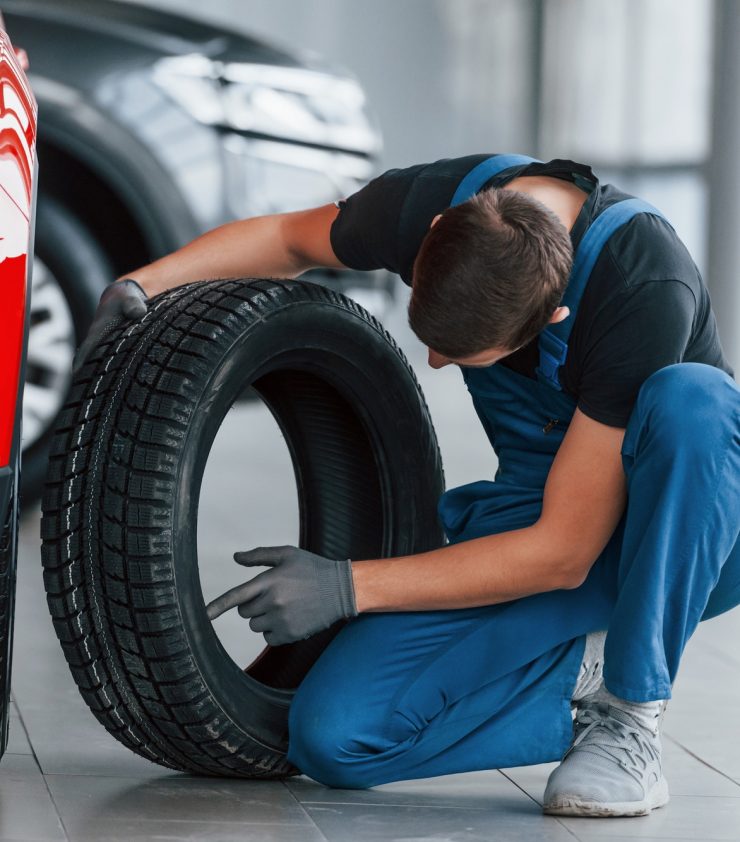 Man in uniform changing tire of automobile. Conception of car service